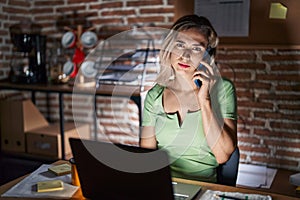 Young beautiful woman working at the office at night speaking on the phone looking sleepy and tired, exhausted for fatigue and