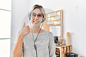 Young beautiful woman working at the office wearing operator headset smiling happy and positive, thumb up doing excellent and