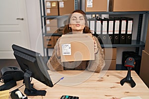 Young beautiful woman working at small business ecommerce holding box looking at the camera blowing a kiss being lovely and sexy