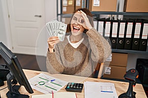 Young beautiful woman working at small business ecommerce holding money smiling happy doing ok sign with hand on eye looking