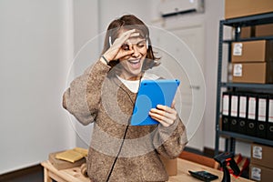 Young beautiful woman working at small business ecommerce smiling happy doing ok sign with hand on eye looking through fingers