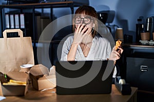 Young beautiful woman working using computer laptop and eating delivery food bored yawning tired covering mouth with hand