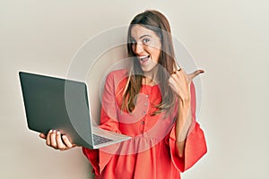 Young beautiful woman working using computer laptop pointing thumb up to the side smiling happy with open mouth