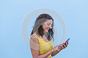 Young beautiful woman in yellow dress using mobile phone over a blue wall. Outdoors. Travel concept. City
