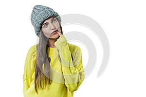 Young beautiful woman in yellow sweater and gray big loop knitted beanie hat, thoughtful holding a finger near her lips, on white