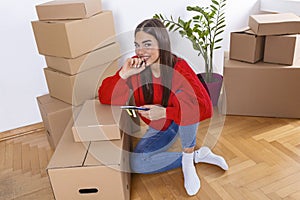 A young beautiful women makes her notes and plans in her new flat,apartment. Young woman packing cardboard box. Moving house