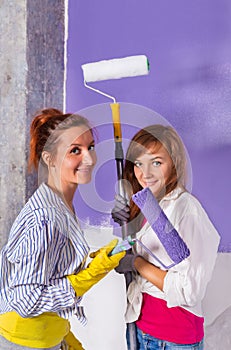 Young beautiful women paints white wall with purple paint roller