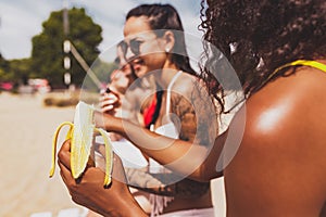 Young beautiful women in swimsuits resting on the beach, drinking cool drinks, having fun, sunbathing