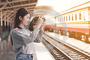 Young beautiful women traveler using a camera shooting a photo at the train station while waiting the train going up country