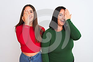 Young beautiful women wearing casual clothes standing over isolated white background covering one eye with hand, confident smile