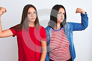 Young beautiful women wearing casual clothes standing over isolated white background Strong person showing arm muscle, confident