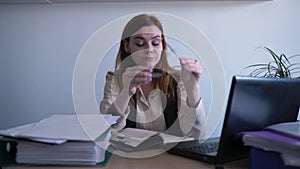 Young beautiful working woman is very tired takes off glasses and rubbing tired eyes sitting at table with laptop in