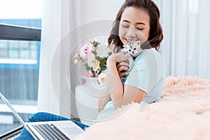 Young beauty Asian woman working on laptop at apartment condominium home with kitten cat pet.