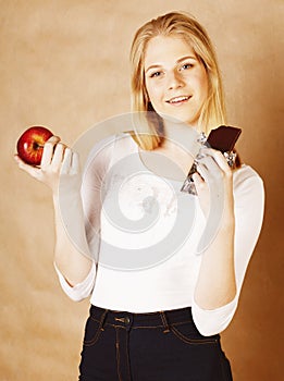 Young beauty blond teenage girl eating chocolate smiling, choice between sweet and apple