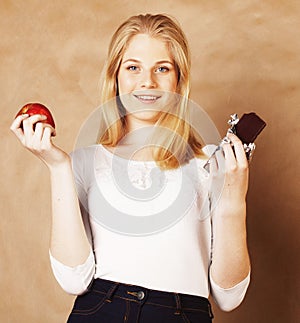Young beauty blond teenage girl eating chocolate smiling, choice between sweet and apple
