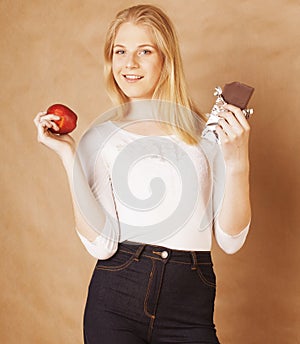 Young beauty blond teenage girl eating chocolate smiling, choice between sweet and apple