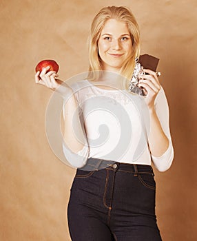 young beauty blond teenage girl eating chocolate smiling, choice between sweet and apple