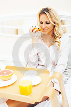 Young beauty blond woman having breakfast in bed early sunny morning, princess house interior room, healthy lifestyle