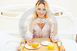 Young beauty blond woman having breakfast in bed early sunny morning, princess house interior room, healthy lifestyle