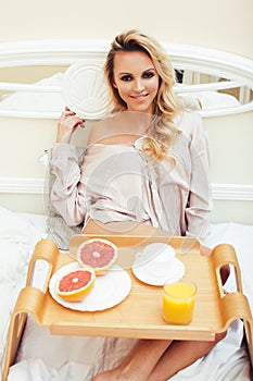 Young beauty blond woman having breakfast in bed early sunny morning, princess house interior room, healthy lifestyle