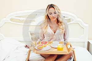 Young beauty blond woman having breakfast in bed early sunny morning, princess house interior room, healthy lifestyle