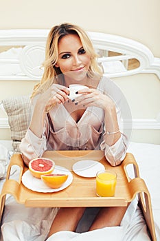 Young beauty blond woman having breakfast in bed early sunny morning, princess house interior room, healthy lifestyle