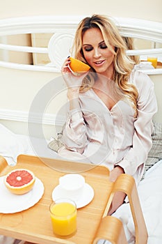 Young beauty blond woman having breakfast in bed early sunny morning, princess house interior room, healthy lifestyle