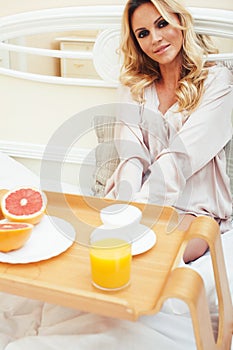 Young beauty blond woman having breakfast in bed early sunny morning, princess house interior room, healthy lifestyle