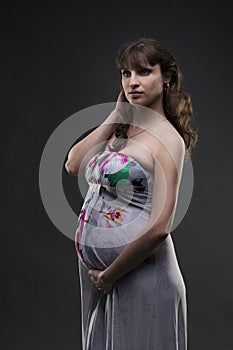 Young beauty and caucasian pregnant woman in sundress on gray studio background