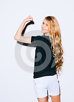 Young beauty fitness blonde woman showing her muscles, her back to the camera, long hair and smiling. Indoor. Warm color.