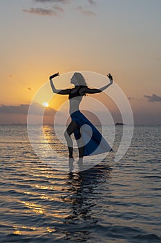 Young beauty girl dancing at tropical beach on sea water at paradise island at sunset. Summer concept