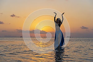 Young beauty girl dancing at tropical beach on sea water at paradise island at sunset. Summer concept