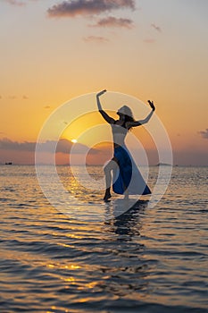 Young beauty girl dancing at tropical beach on sea water at paradise island at sunset. Summer concept