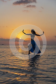 Young beauty girl dancing at tropical beach on sea water at paradise island at sunset. Summer concept