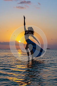 Young beauty girl dancing at tropical beach on sea water at paradise island at sunset. Summer concept. Holiday travel