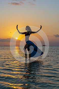 Young beauty girl dancing at tropical beach on sea water at paradise island at sunset. Summer concept. Holiday travel