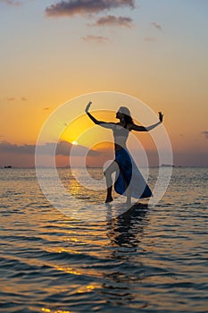 Young beauty girl dancing at tropical beach on sea water at paradise island at sunset. Summer concept. Holiday travel