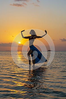 Young beauty girl dancing at tropical beach on sea water at paradise island at sunset. Summer concept. Holiday travel