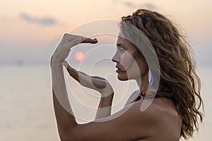 Young beauty girl at tropical beach holds hands around the sun at paradise island at sunset, closeup. Summer concept. Holiday