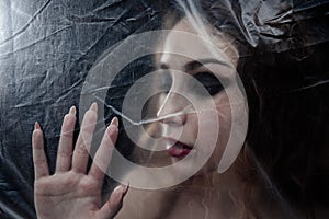 Young beauty sad woman trapped behind a plastic sheet as protection against COVID-19