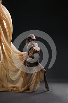 Young beauty and caucasian pregnant woman with yellow silk on gray studio background