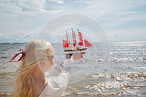 Young beauty woman holding red sail boat against sea and sky. Romantic vacation concept