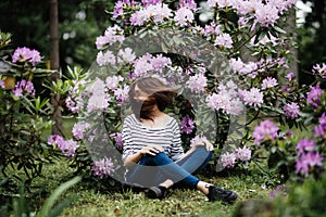 Young beauty woman play waving with hait sitting surrounded of purple flowers outdoors in the park