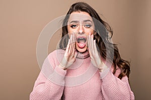 Young beauty woman shout and scream using her hands as tube, studio shoot isolated on brown