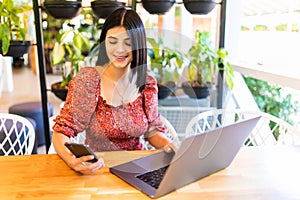 Young beauty woman sitting in coffee shop at table, drinking coffee and using smartphone