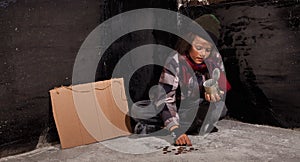 Young beggar boy counting coins - sitting on the ground