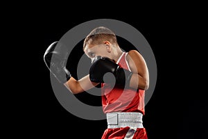 Young beginner boxer, sportive boy training isolated over dark background. Concept of sport, movement, studying