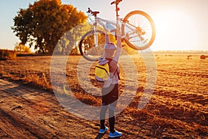 Young bicyclist raising her bicycle in autumn field. Happy woman celebrates victory holding bike in hands