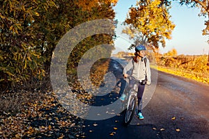 Young bicyclist riding in autumn field at sunset. Happy woman smiling