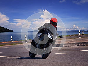 young biker man riding motorcycle on asphalt road against beautiful sea water background